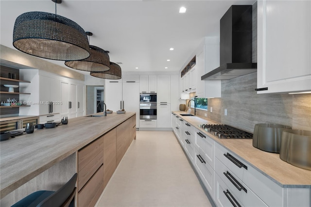 kitchen featuring white cabinets, pendant lighting, wall chimney range hood, and stainless steel appliances