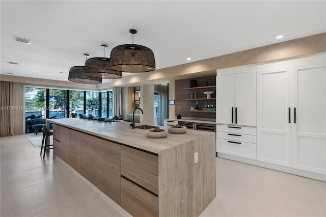 kitchen featuring a breakfast bar, sink, an island with sink, decorative light fixtures, and white cabinetry