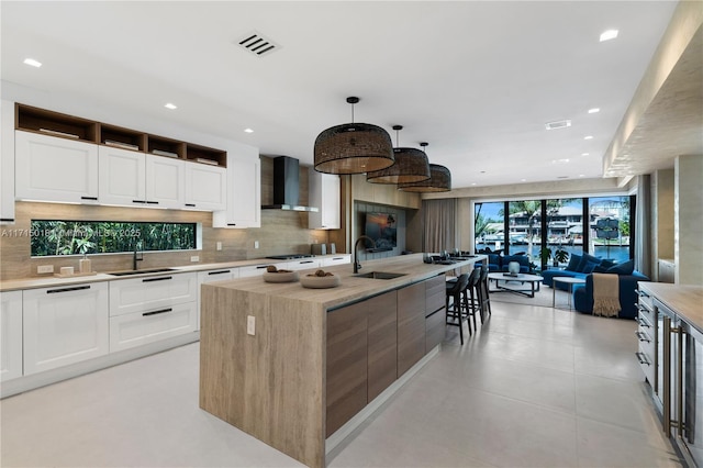 kitchen with white cabinets, decorative light fixtures, wall chimney exhaust hood, and a spacious island