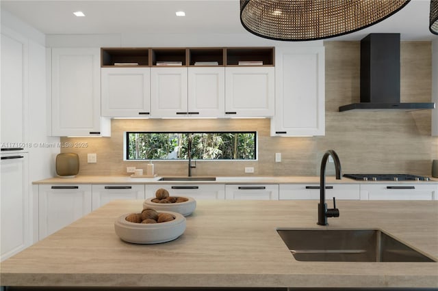 kitchen with backsplash, stainless steel gas cooktop, wall chimney exhaust hood, and sink