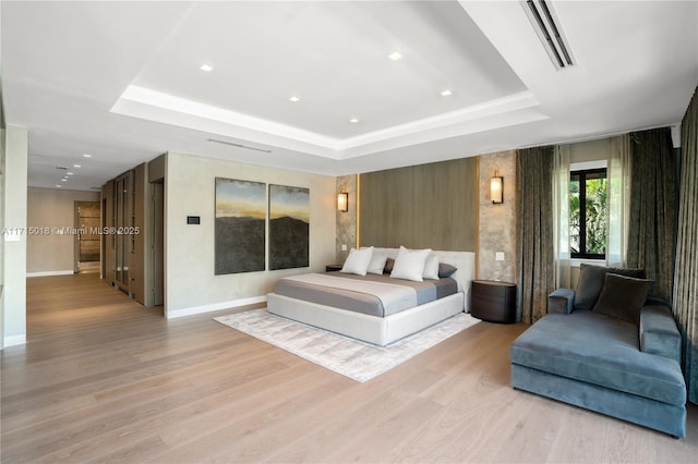 bedroom with light wood-type flooring and a raised ceiling