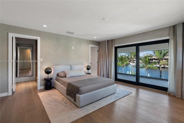 bedroom featuring access to exterior, a water view, and light hardwood / wood-style flooring