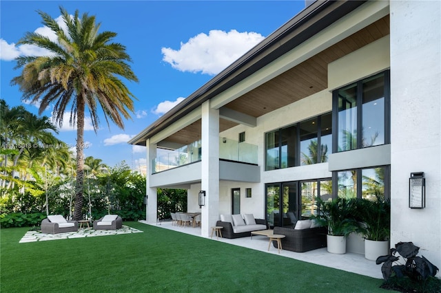 rear view of property featuring a lawn, an outdoor living space, a balcony, and a patio