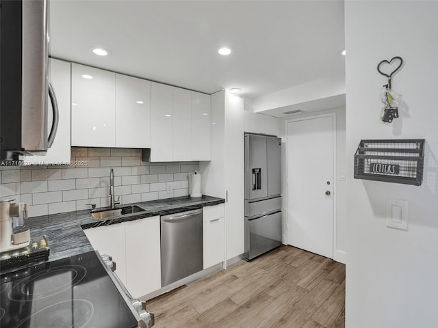 kitchen with appliances with stainless steel finishes, tasteful backsplash, sink, light hardwood / wood-style flooring, and white cabinets