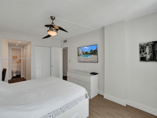 bedroom with ensuite bathroom, ceiling fan, a textured ceiling, wood-type flooring, and a closet