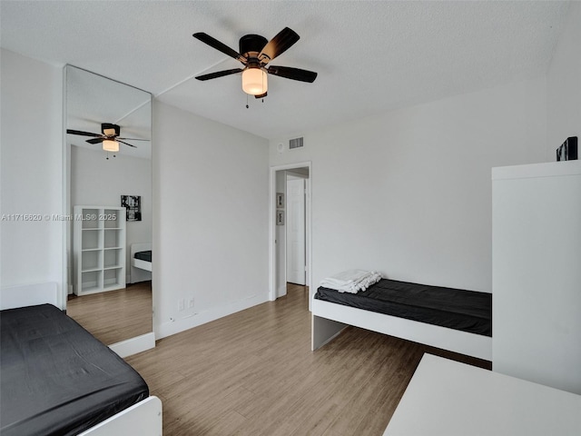 bedroom with ceiling fan, wood-type flooring, and a textured ceiling