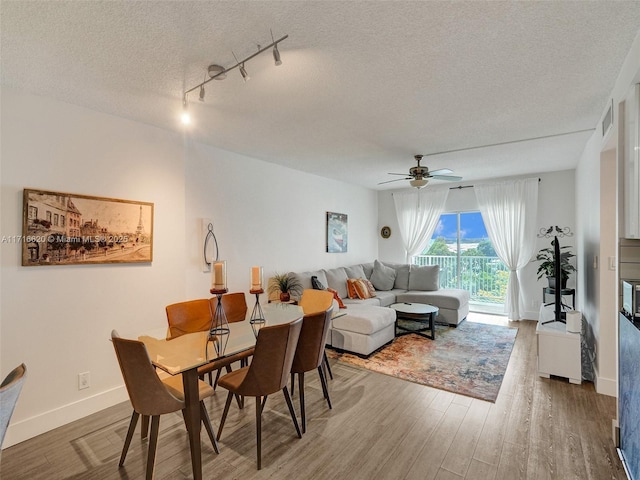 dining area with rail lighting, ceiling fan, wood-type flooring, and a textured ceiling