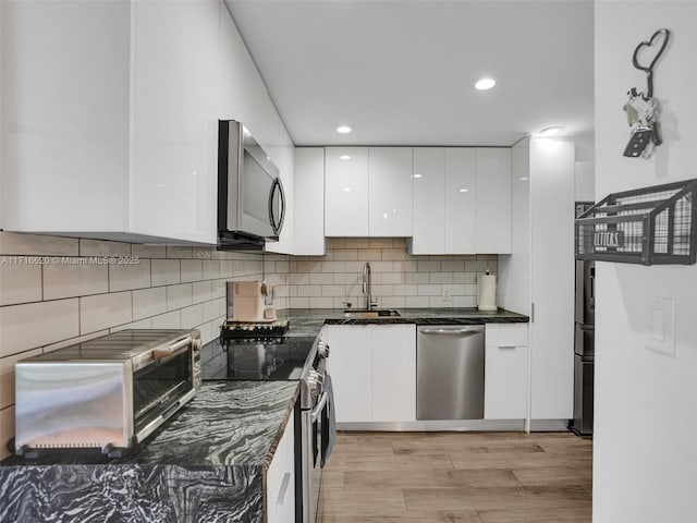 kitchen featuring white cabinetry, sink, dark stone counters, decorative backsplash, and appliances with stainless steel finishes