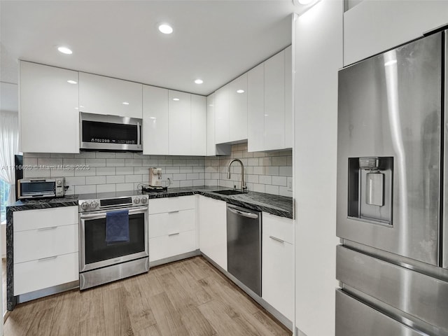 kitchen featuring tasteful backsplash, stainless steel appliances, sink, light hardwood / wood-style flooring, and white cabinets