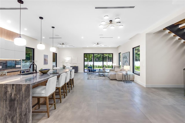 kitchen featuring a kitchen bar, ceiling fan, sink, pendant lighting, and dark stone countertops