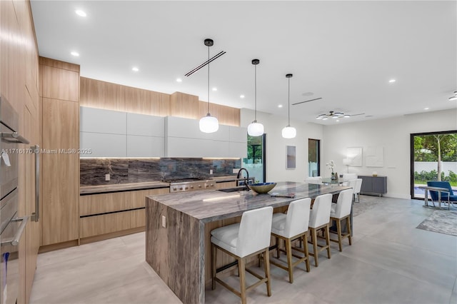 kitchen featuring white cabinetry, a large island, sink, dark stone counters, and decorative light fixtures