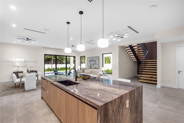 kitchen featuring pendant lighting, sink, a kitchen island with sink, and stone counters