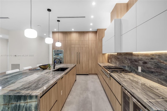 kitchen with appliances with stainless steel finishes, light stone counters, sink, white cabinetry, and hanging light fixtures