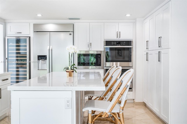 kitchen with white cabinets, a kitchen island with sink, built in appliances, and wine cooler