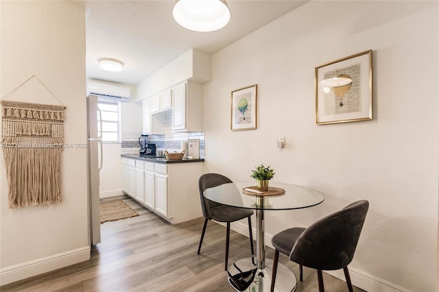 kitchen featuring decorative backsplash, white cabinetry, light hardwood / wood-style floors, and a wall mounted air conditioner