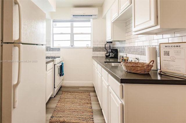 kitchen featuring white appliances, an AC wall unit, tasteful backsplash, white cabinets, and sink