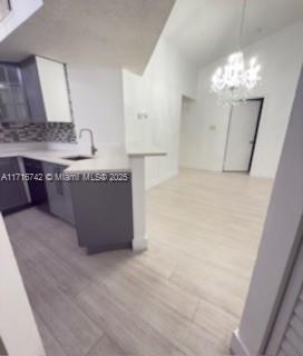 kitchen with white cabinetry, sink, a notable chandelier, light hardwood / wood-style floors, and decorative light fixtures