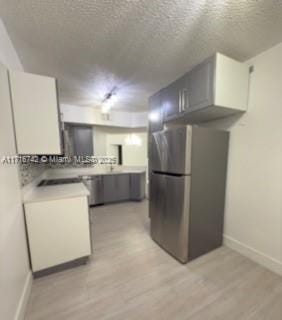 kitchen featuring appliances with stainless steel finishes, a textured ceiling, light hardwood / wood-style floors, and gray cabinetry