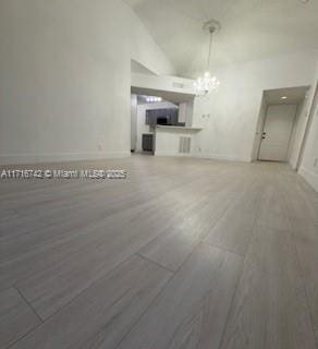 unfurnished living room with a chandelier, dark hardwood / wood-style floors, and vaulted ceiling