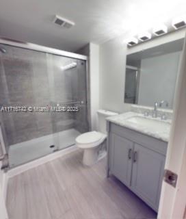 bathroom featuring a shower with door, vanity, wood-type flooring, and toilet