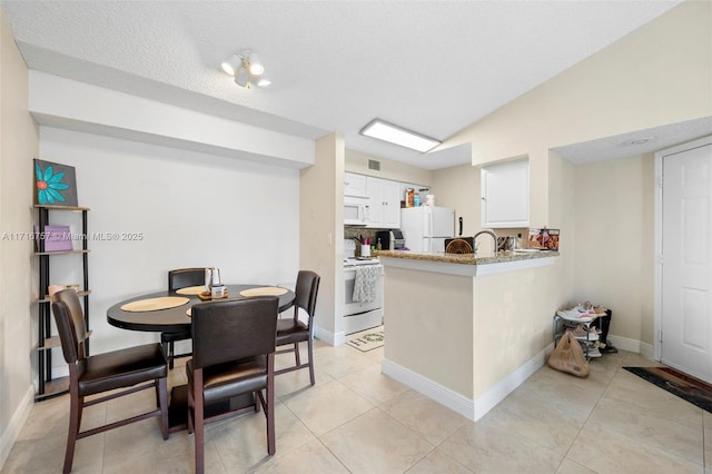 kitchen with white appliances, kitchen peninsula, vaulted ceiling, light stone countertops, and white cabinetry