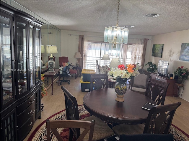 dining area featuring a textured ceiling, an inviting chandelier, and light hardwood / wood-style flooring