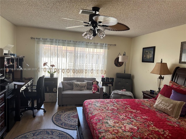 bedroom with ceiling fan, wood-type flooring, a textured ceiling, and multiple windows