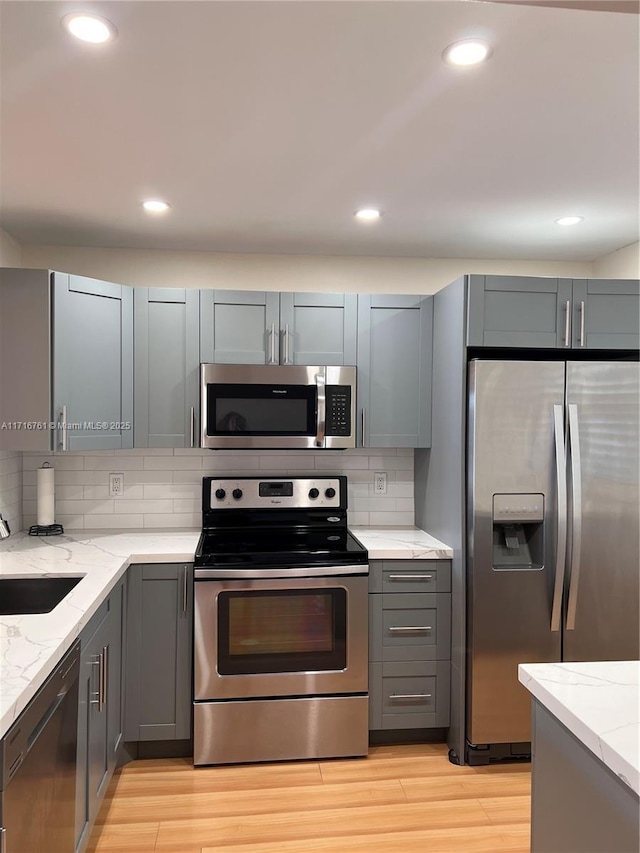 kitchen featuring backsplash, gray cabinetry, light stone countertops, and appliances with stainless steel finishes