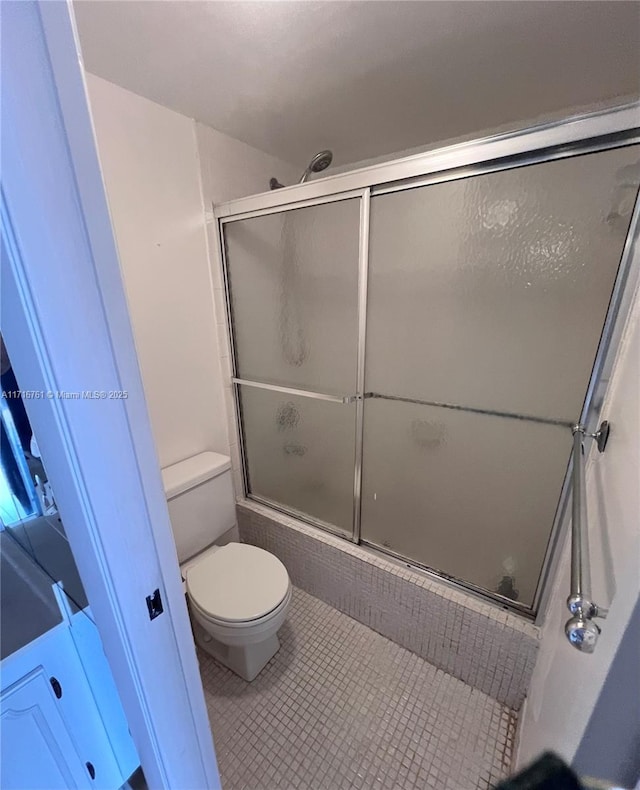 bathroom with tile patterned flooring, enclosed tub / shower combo, and toilet