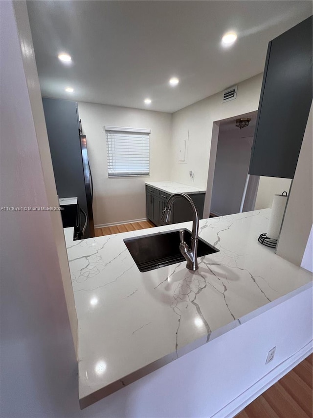 kitchen with light stone countertops, kitchen peninsula, sink, and light hardwood / wood-style flooring