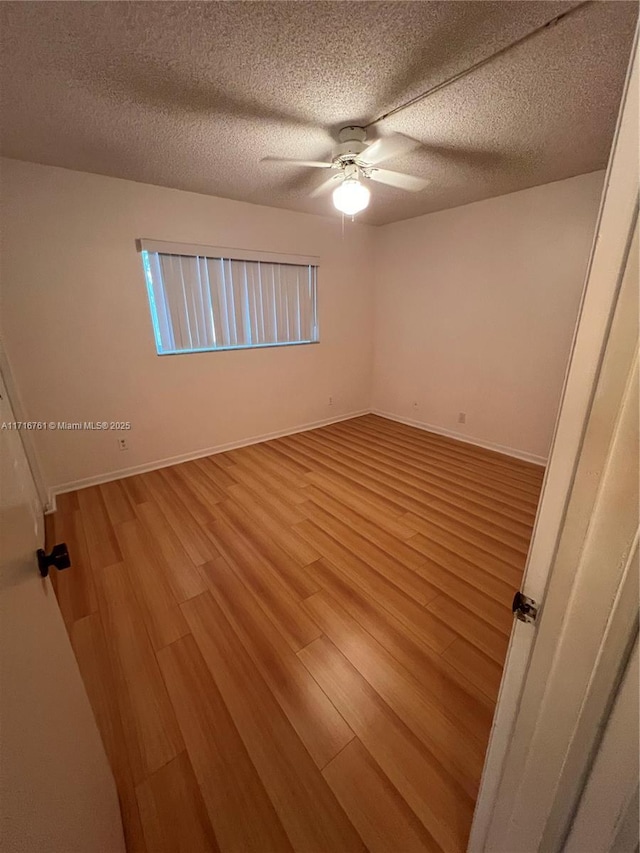 empty room featuring ceiling fan, light wood-type flooring, and a textured ceiling