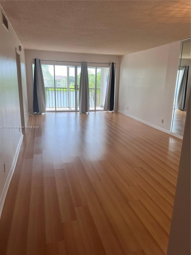 empty room with a textured ceiling and light hardwood / wood-style flooring