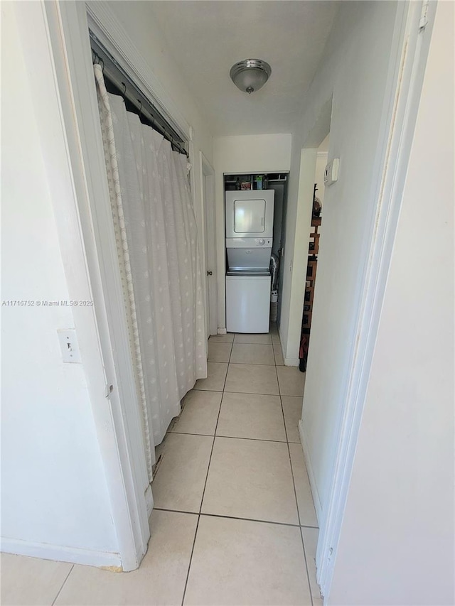 corridor with light tile patterned floors and stacked washer and clothes dryer