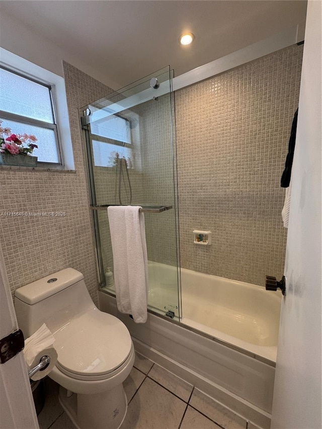 bathroom with tile patterned floors, toilet, combined bath / shower with glass door, and tile walls