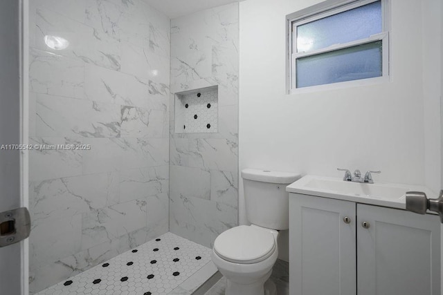 bathroom with a tile shower, vanity, and toilet