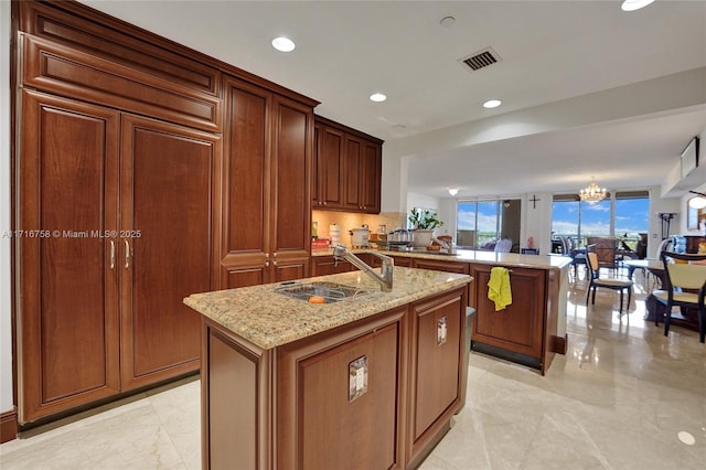 kitchen featuring light stone countertops, sink, an inviting chandelier, kitchen peninsula, and a center island with sink