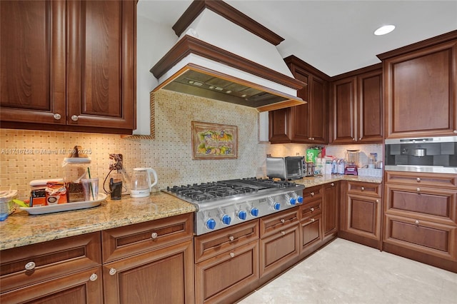 kitchen with decorative backsplash, light stone countertops, premium range hood, and stainless steel gas cooktop