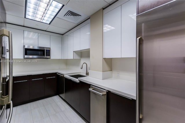 kitchen with dark brown cabinets, a paneled ceiling, stainless steel appliances, and sink