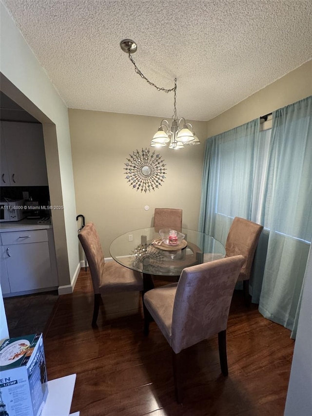 dining area featuring dark wood-type flooring, a chandelier, and a textured ceiling