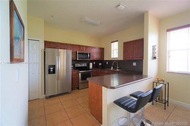 kitchen featuring light tile patterned flooring, a peninsula, stainless steel appliances, and a kitchen bar