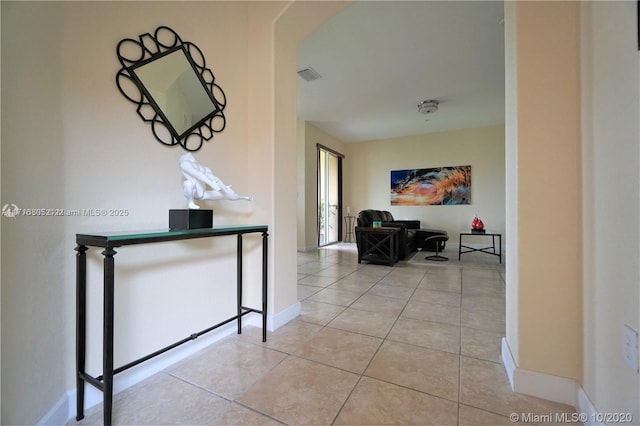 corridor featuring light tile patterned floors, visible vents, arched walkways, and baseboards