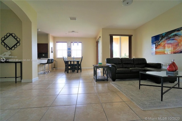 living room featuring light tile patterned flooring, visible vents, arched walkways, and baseboards