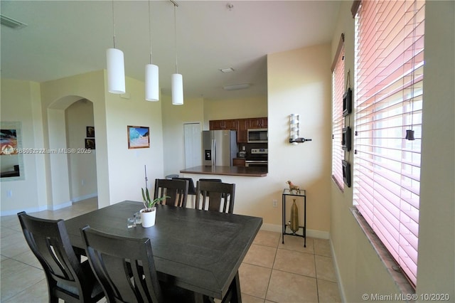 dining space with light tile patterned floors, visible vents, arched walkways, and baseboards