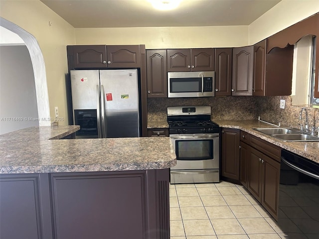 kitchen featuring arched walkways, dark brown cabinetry, a sink, appliances with stainless steel finishes, and backsplash