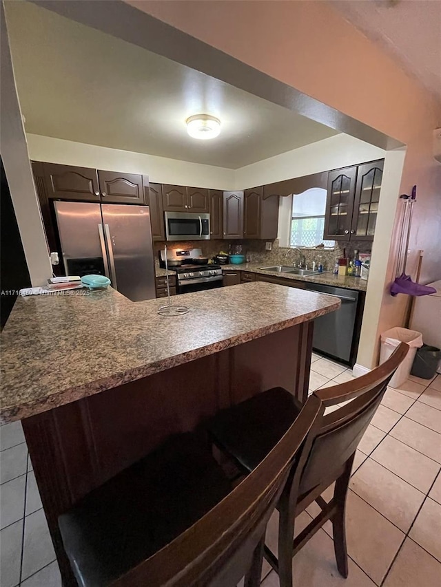 kitchen featuring tasteful backsplash, a breakfast bar, stainless steel appliances, a sink, and light tile patterned flooring