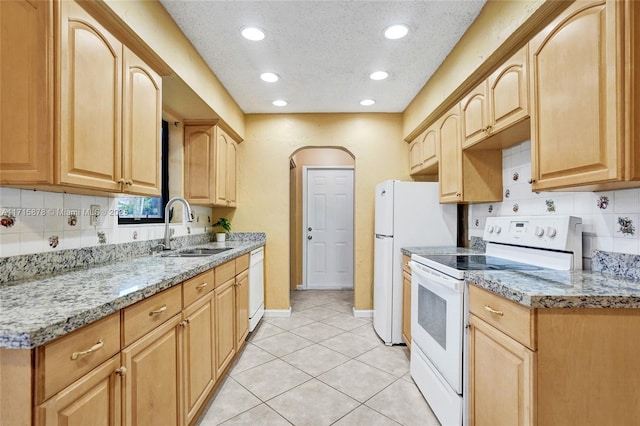 kitchen with white appliances, sink, decorative backsplash, light brown cabinetry, and light stone counters