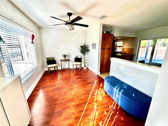 living area with a textured ceiling, hardwood / wood-style flooring, ceiling fan, and a healthy amount of sunlight