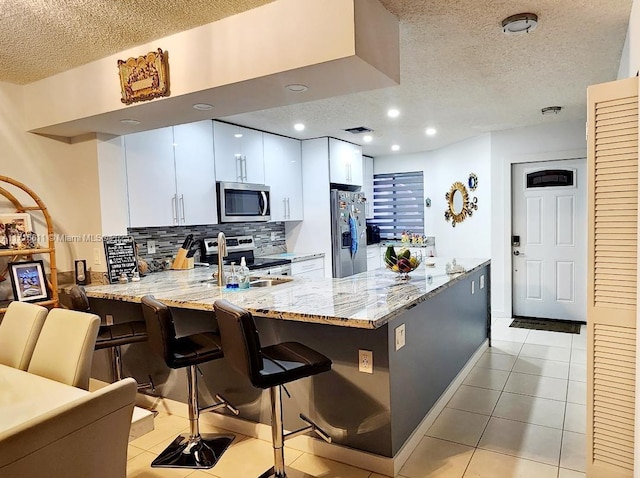 kitchen featuring kitchen peninsula, white cabinetry, light tile patterned floors, and stainless steel appliances