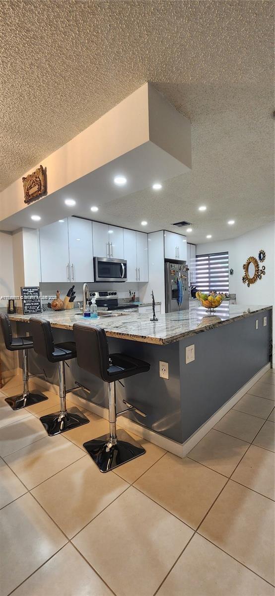 kitchen featuring white cabinetry, a kitchen breakfast bar, light stone counters, kitchen peninsula, and appliances with stainless steel finishes