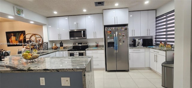 kitchen featuring white cabinets, kitchen peninsula, appliances with stainless steel finishes, and dark stone counters